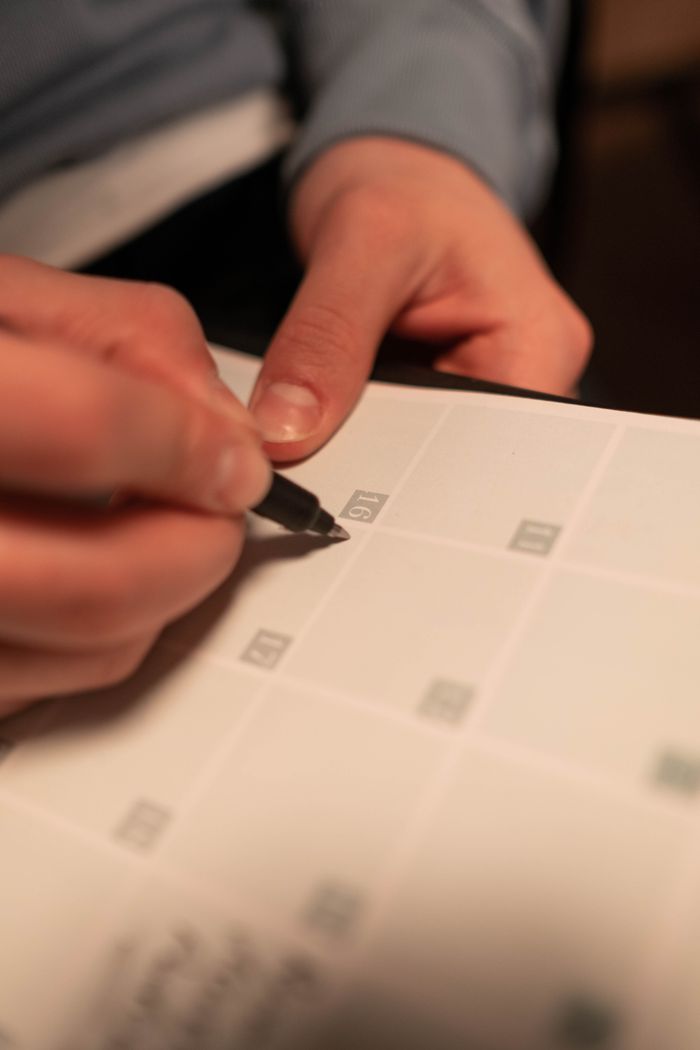 Close-up of a hand writing on a calendar, planning future events.